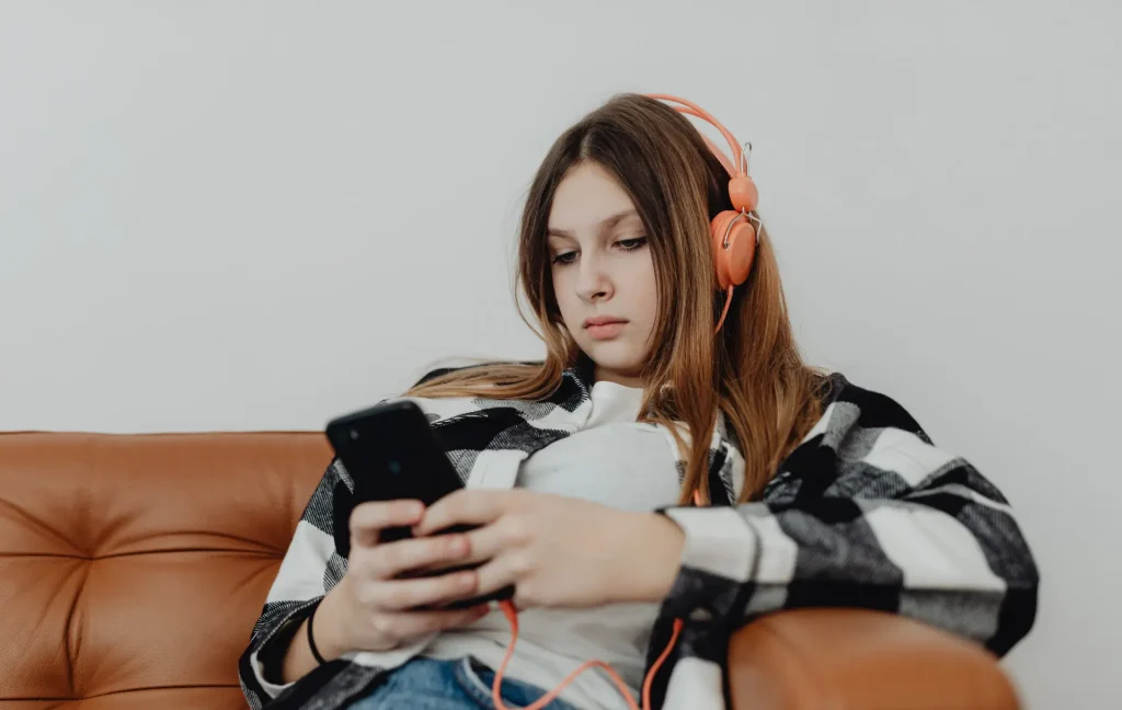 student at home spending free time on phone, with headphones on