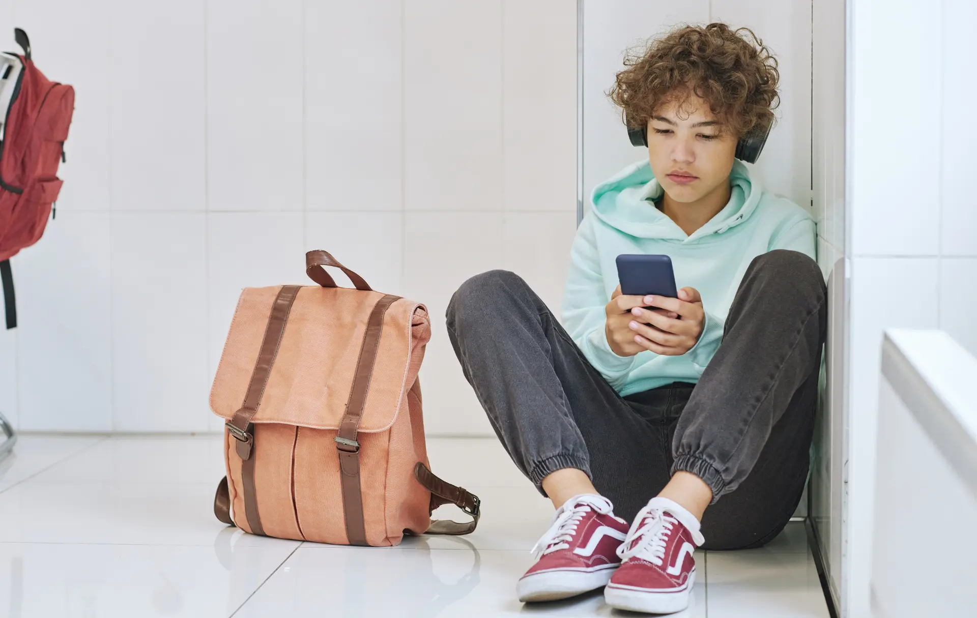 header_technology role in wellbeing student sitting in school hallway, using phone