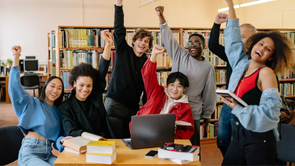 high school student group of different races and genders in library cheering on something