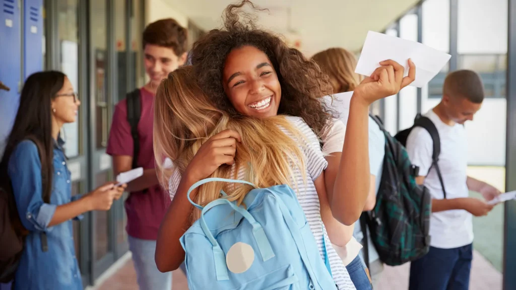 happy students hugging outside of school, smiling with other students in the background