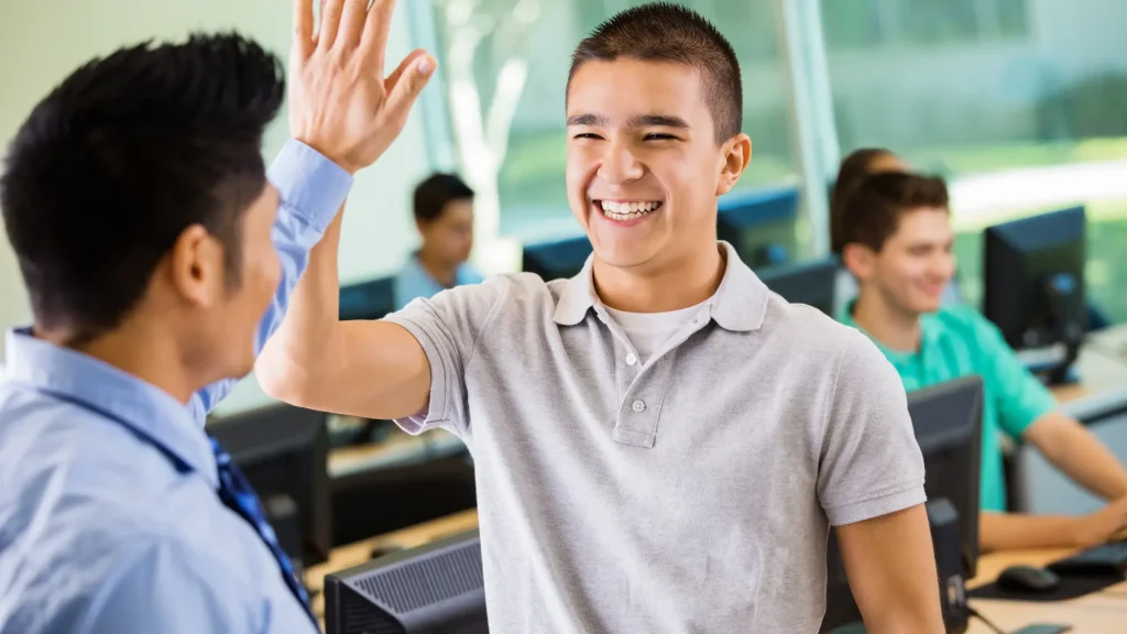 highschool male student visibly happy highfiving male teacher in class