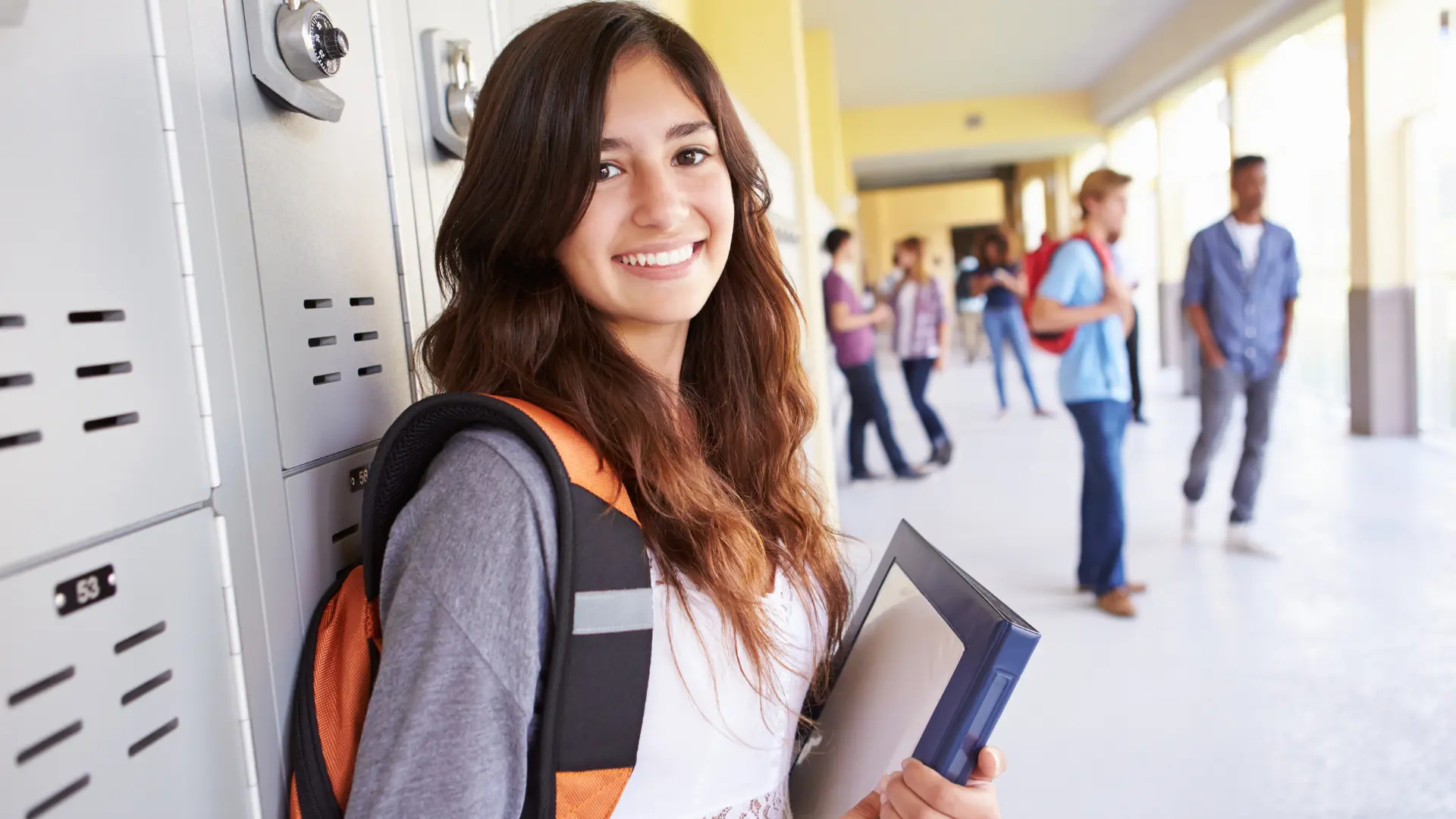 happy high school female student stands in hallway smiling at camera with books in her hand