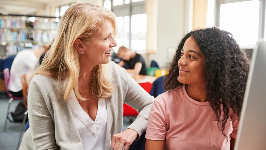 female high school student with female older blonde teacher or headteacher at computer, getting encouraged