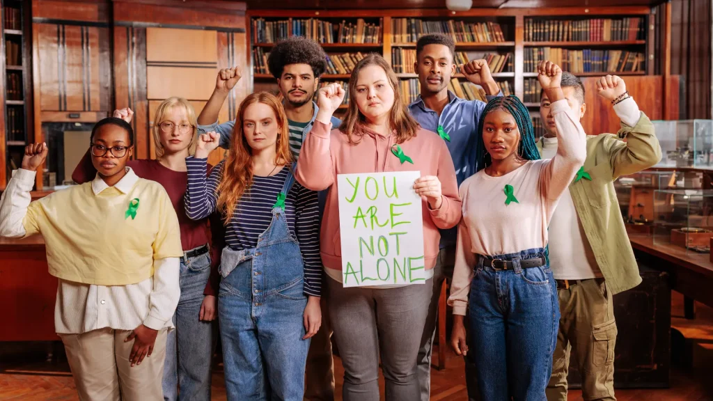 student group in darker room with sign reading "you are not alone" and showing gestures of support